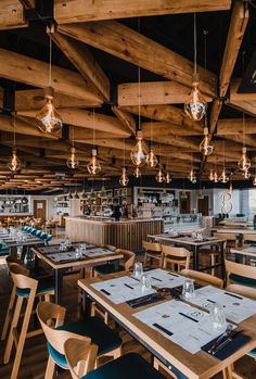 an empty restaurant with wooden tables and blue chairs, hanging lights and chandeliers