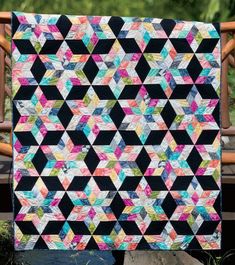 a black and white quilt with multicolored triangles on it in front of a wooden bench