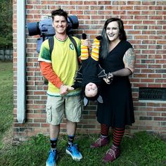 a man and woman standing next to each other in front of a brick wall holding items