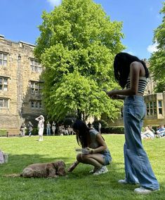 two women are sitting on the grass in front of a building and one is petting her dog