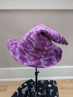 A handmade crochet witch hat made with purple mottled acrylic yarn. Made to be slouchy and comfy, with a moldable wire brim. Cozy muted purples ranging from lavender to deep eggplant.  Hat has a 11" diameter straight across the brim at the widest point. The inside circumference is roughly 20-22" - it can stretch a bit. Pattern: TheEntangledFae - https://www.etsy.com/shop/TheEntangledFae Hand Knitted Purple Hat One Size, Hand Knitted Purple Hat, Hand Knitted One Size Purple Hats, Hand-knitted One Size Purple Hat, Adjustable Purple Crochet Yarn Hat, Adjustable Purple Yarn Crochet Hat, Purple Crochet Yarn Hat, Purple Yarn Beanie Hat, Hand Knitted Purple Yarn Hats