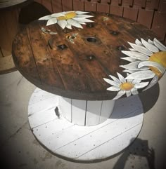 a wooden table with white flowers painted on the top and bottom, sitting in front of a fence