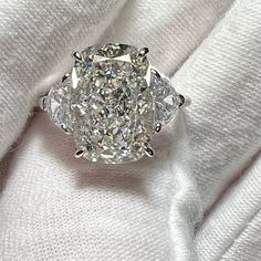 an oval cut diamond sits on top of a white blanket, surrounded by two smaller round diamonds