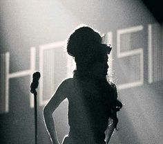 a woman standing in front of a microphone with her hands on her hips while holding a guitar