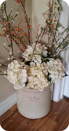 a white bucket with flowers in it sitting on a wooden floor next to a wall