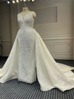 a white wedding dress on display in a room with lights hanging from the ceiling and two mannequins behind it