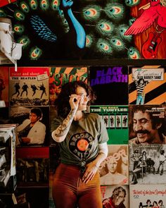 a woman standing in front of a wall covered with posters