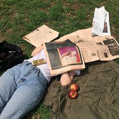 a person laying on the ground reading a newspaper and an apple next to them,