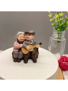 a small figurine of two people sitting on top of a table next to a vase