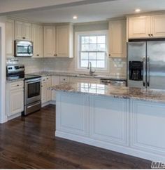 an empty kitchen with white cabinets and granite counter tops, stainless steel appliances and wood flooring