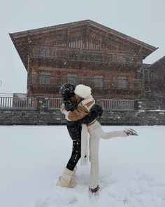 two people are hugging in the snow near a large building with a clock on it