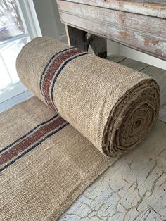 two rolled up rugs sitting on the floor in front of a wooden bench and window