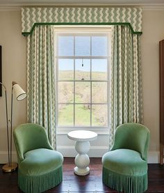 two green chairs and a table in front of a window with curtains on the windowsill