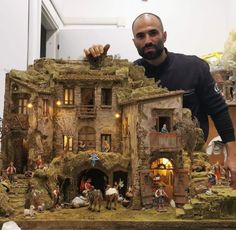 a man standing next to a fake house made out of clay with figures on it