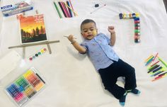 a little boy laying on top of a table with crayons and markers in front of him