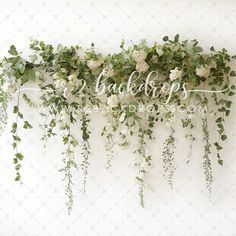 some white flowers and greenery are hanging on the wall