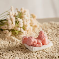 there is a small pink figurine on top of a white blanket next to flowers