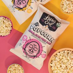 three bags of popcorn sitting next to two bowls of cereal on a pink and yellow surface