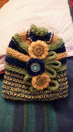 a crocheted hat with flowers on it sitting on top of a bed next to a pillow