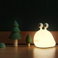 a lamp that looks like a frog with eyes on it's face and two trees in the background