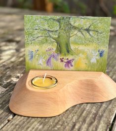 a card with a candle in it sitting on a wooden table next to a tree