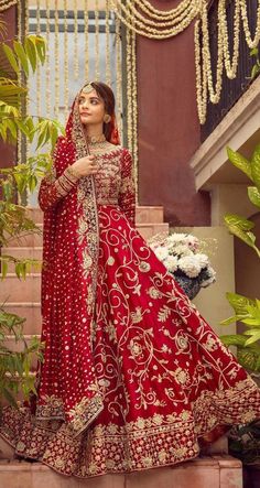 a woman in a red and gold bridal gown standing on steps with greenery