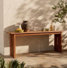 a wooden table sitting on top of a patio next to a potted plant and vase