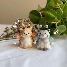 two small figurines sitting next to each other on a white table with green plants