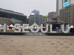 a large sign that says seoul on it in front of some buildings and people walking around