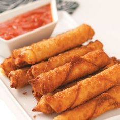 some fried food on a white plate next to a small bowl of tomato dipping sauce