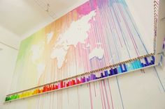 a rainbow colored wall hanging on the side of a building with a world map in the background