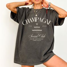 Pop the bubbly on your style with this adorable personalized Champagne Social Club tee!   This comfy, customizable tee is perfect for celebrating any occasion with a touch of fizz.  Whether it's a girls' night out, a fancy brunch, or just because it's Tuesday, this shirt is ready to clink glasses with some fun. Here's the bubbly brilliance: Two Fizz-tastic Designs: Choose from a glamorous champagne tower or two clinking champagne flutes - both guaranteed to add a touch of whimsy to your outfit. Your Kind of Bubbly Fun: Personalize it! Add your own custom text, like your squad's name, a hilarious quote about champagne, or even the location of your next bubbly adventure. ️ Comfy & Cute: Made from 100% ring-spun US cotton, this relaxed-fit tee feels as good as it looks. Plus, it's pre-shrunk Party T-shirt With Text Print, Trendy Party T-shirt With Letter Print, Party T-shirt With Text Print And Short Sleeves, Trendy T-shirt With Letter Print For Party, Crew Neck Cotton T-shirt For Party, Cotton Crew Neck T-shirt For Party, Party Slogan Cotton T-shirt, Party Cotton T-shirt With Slogan, Party T-shirt With Letter Print In Relaxed Fit