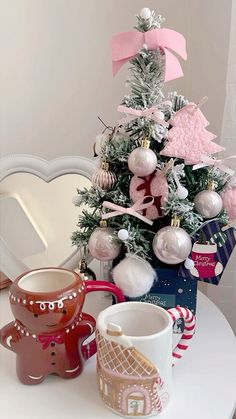 a small christmas tree with ornaments on it and two mugs sitting next to it