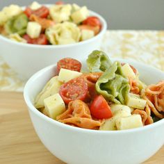 two white bowls filled with pasta and veggies on top of a wooden table