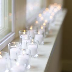 white candles are lined up on a window sill