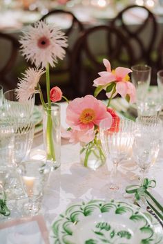 the table is set with pink flowers in vases and glassware, along with other place settings