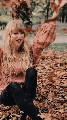 a woman sitting on the ground with her arms in the air and leaves all around her