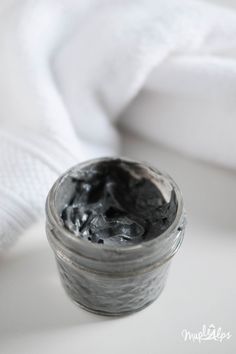 an open jar of black stuff sitting on top of a white table next to a towel