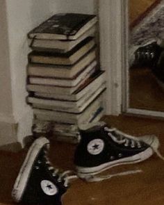 a pile of books sitting on top of a wooden floor next to a pair of black sneakers