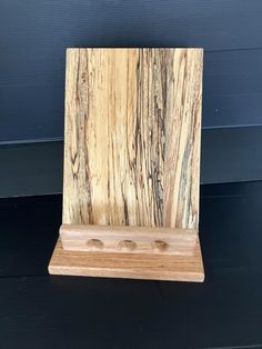 a wooden stand with three holes in it on a black surface next to a blue wall