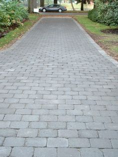 a black car is parked on the side of a brick road in front of some trees