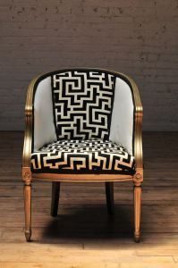 an upholstered chair with black and white designs on it, against a brick wall