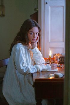 a woman sitting at a table with a candle in front of her and looking off to the side