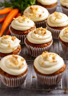 carrot cupcakes with cream cheese frosting and chopped carrots in the background