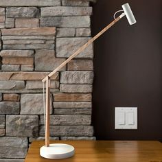 a desk lamp sitting on top of a wooden table next to a brick wall and a light switch