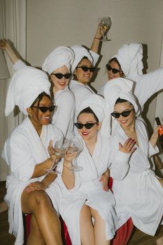 a group of women dressed in white robes and holding wine glasses pose for a photo