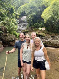 three people are standing in the water near a waterfall and holding onto a stick with one hand