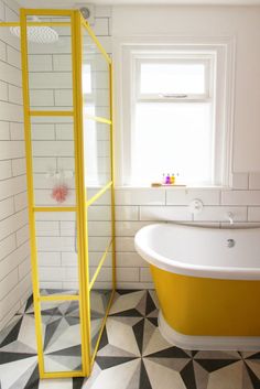 a yellow bath tub sitting next to a window in a white and black tiled bathroom