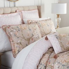 a bed with pink and white comforters in a bedroom next to a mirror on the wall