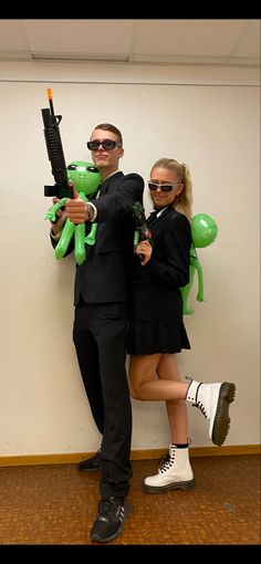 a man and woman dressed in black holding green teddy bears while standing next to each other